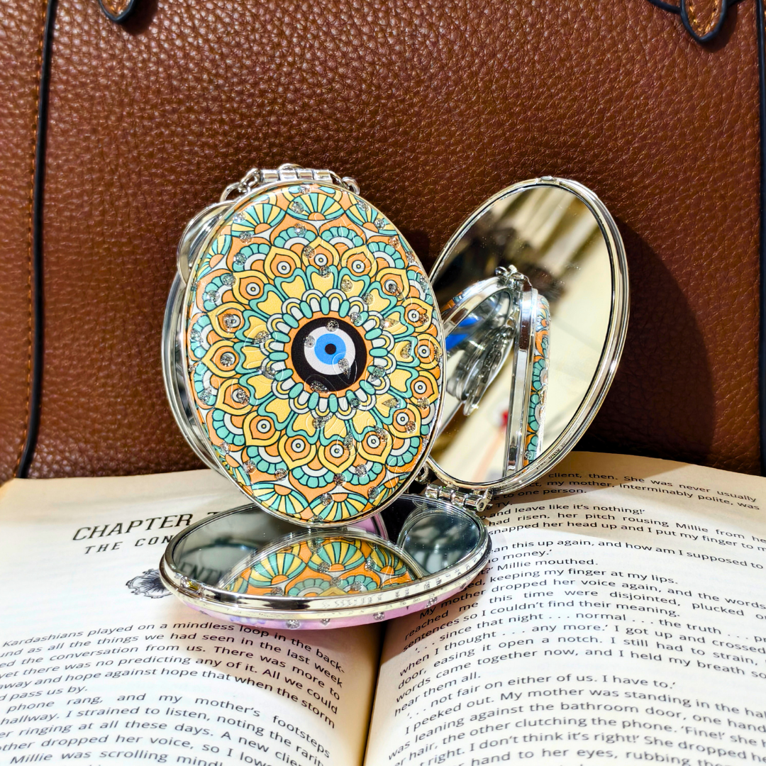 evil eye yellow pocket mirror on top of the book in front of a brown purse