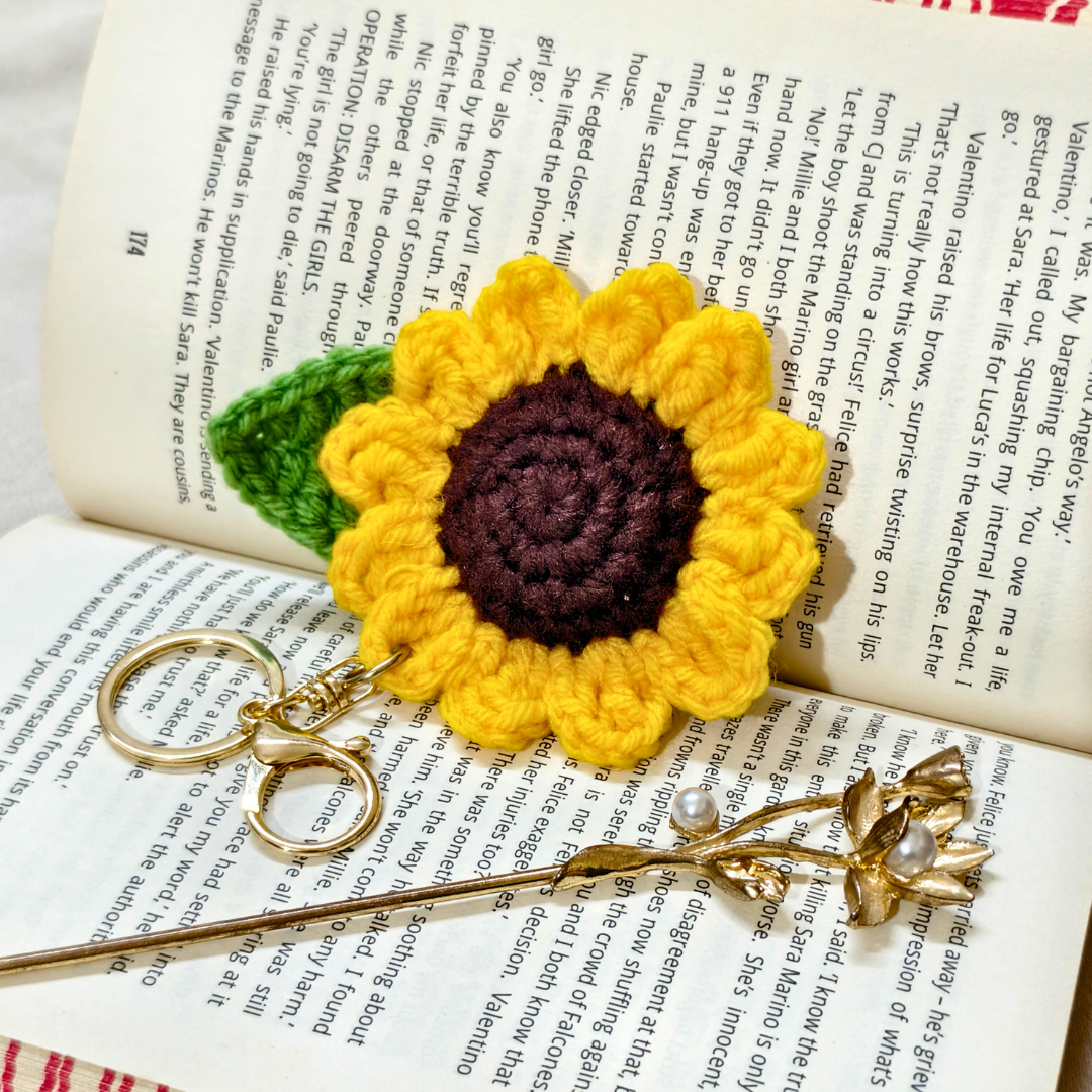crochet sunflower keyring on a book beside a golden bun stick