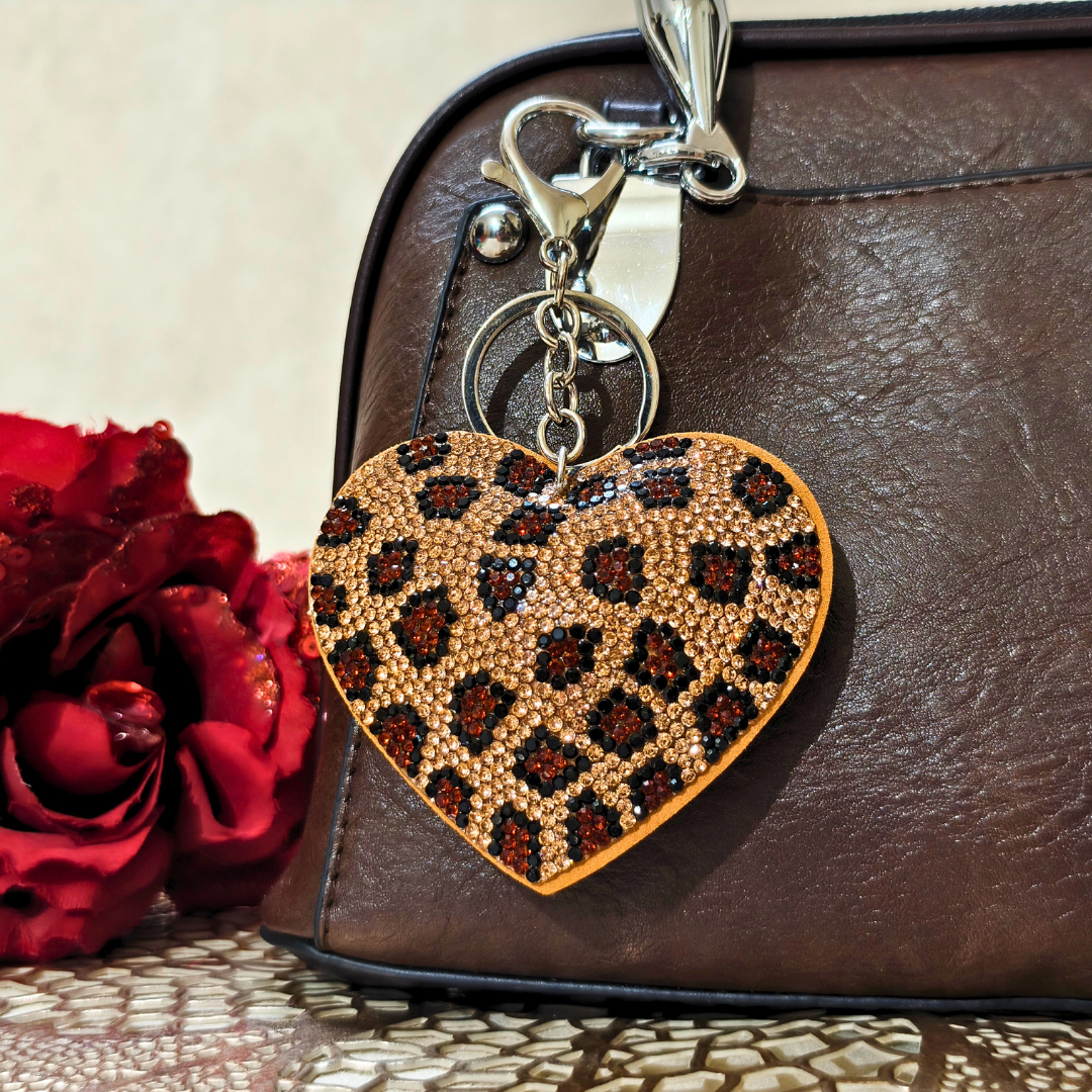 brown heart keychain latched on a brown purse beside a red flower in front of a beige background