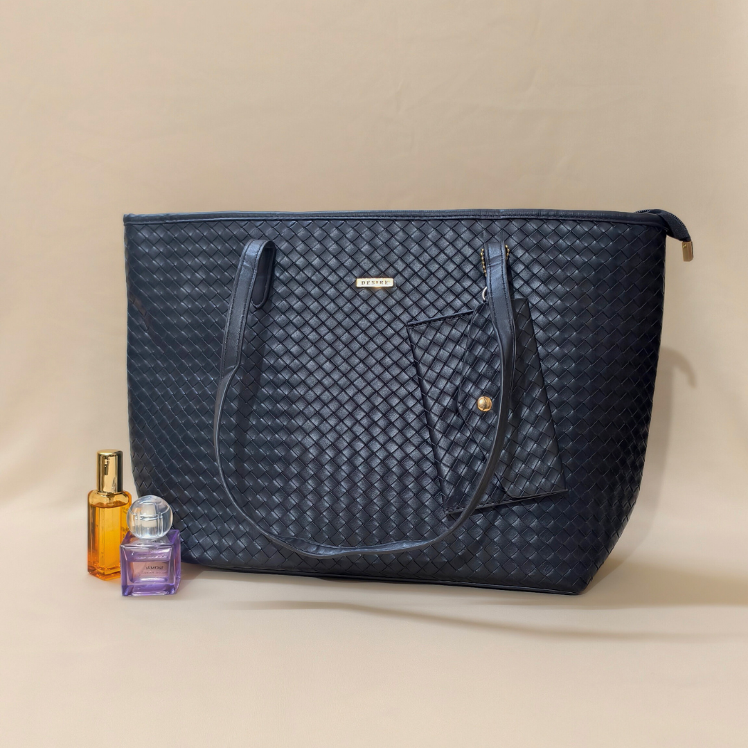Black bag in front of beige background with perfume bottles alongside it.