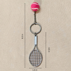 A tennis racket-shaped keychain with a pink tennis ball charm, shown on a beige background with dimension lines indicating a height of 6.5 inches, width of 1.