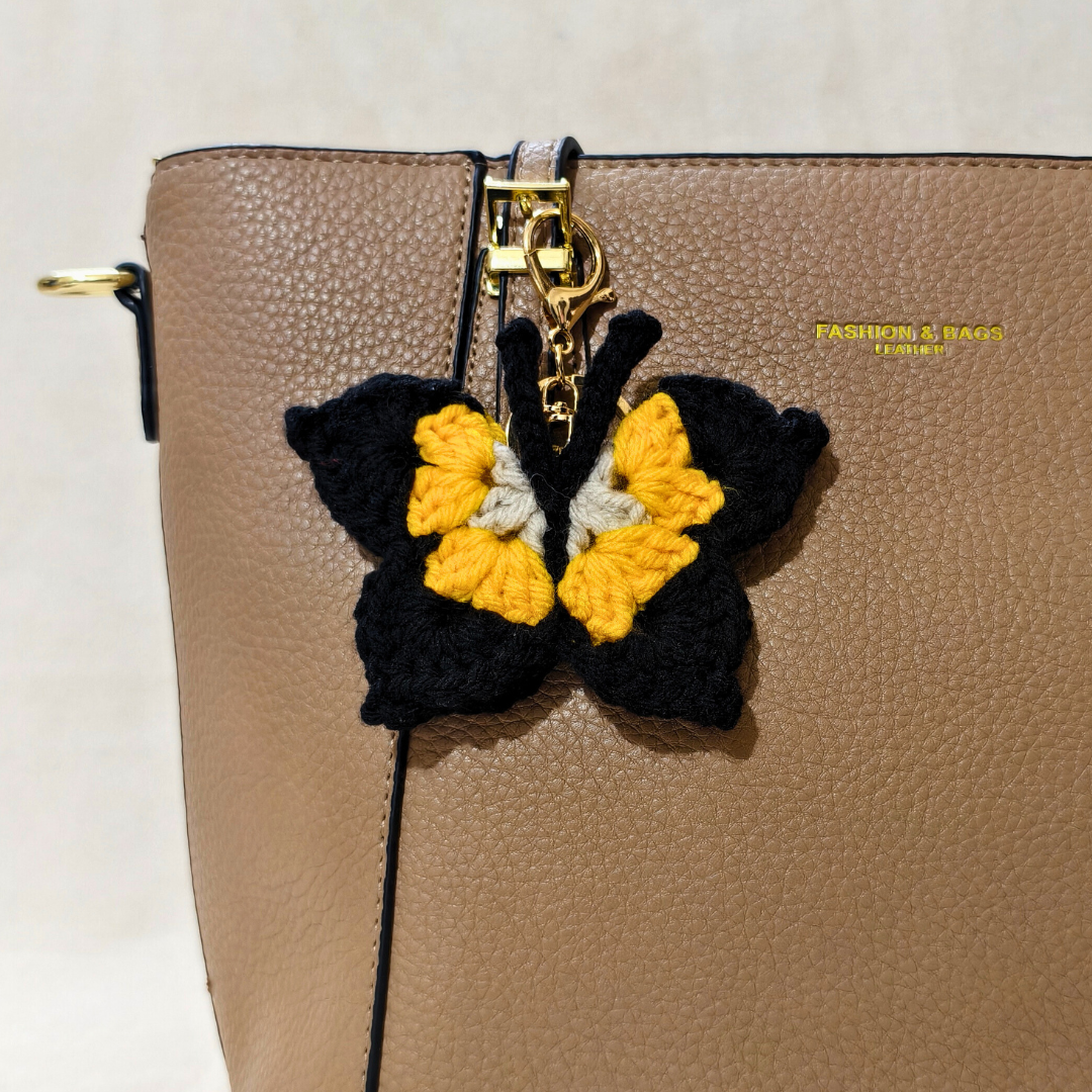 Butterfly-shaped keychain attached to a beige handbag with 'Fashion & Bags' branding.