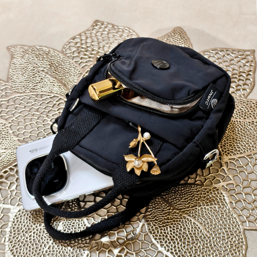 Black crossbody bag with gold accents on a textured surface