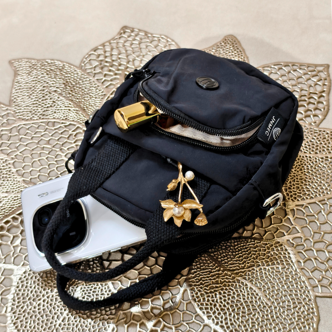 Black crossbody bag with gold accents on a textured surface