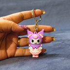 Hand holding a small purple and pink character keychain against a gray background