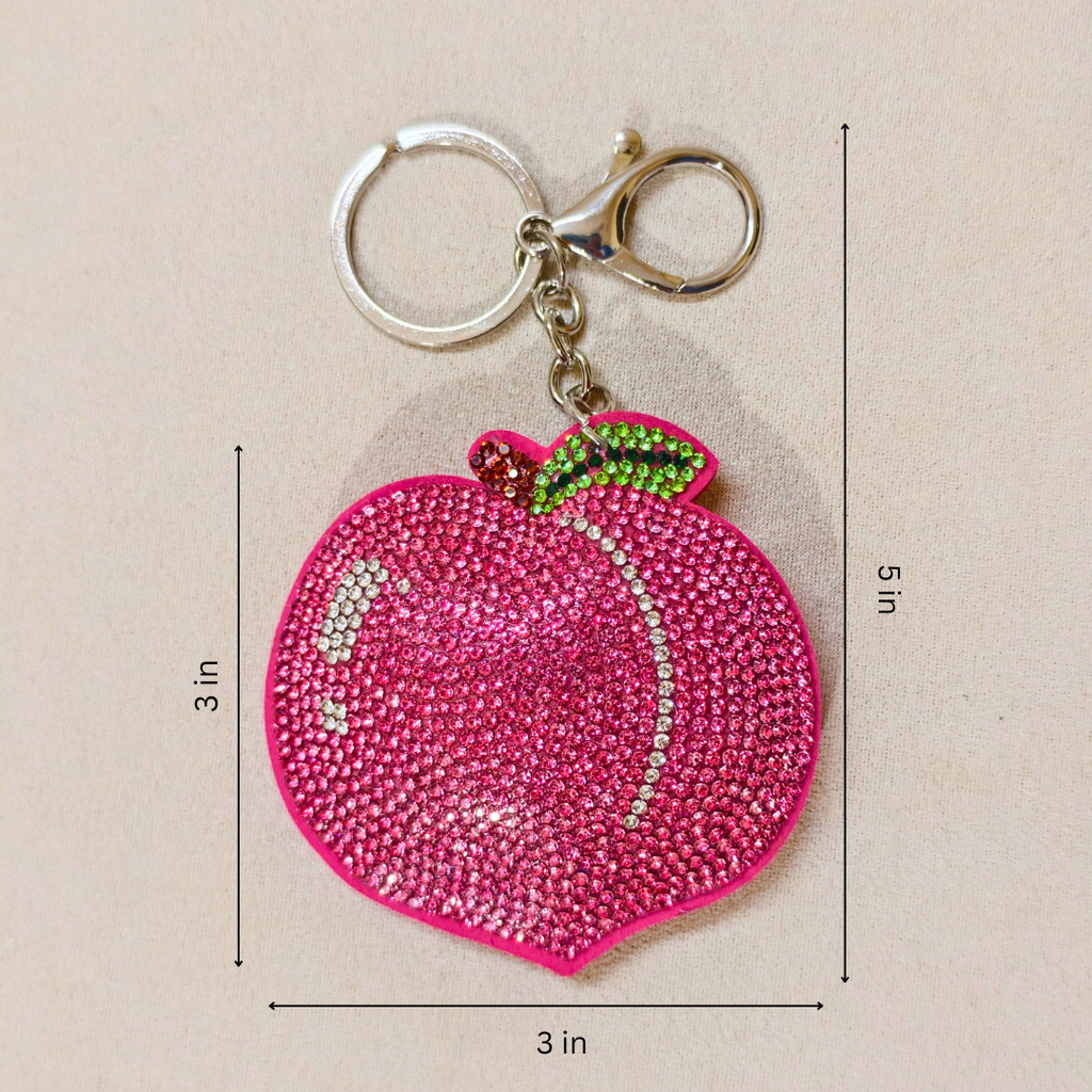 Pink peach-shaped keychain with gemstones on a beige background
