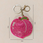 Pink peach-shaped keychain with gemstones on a beige background