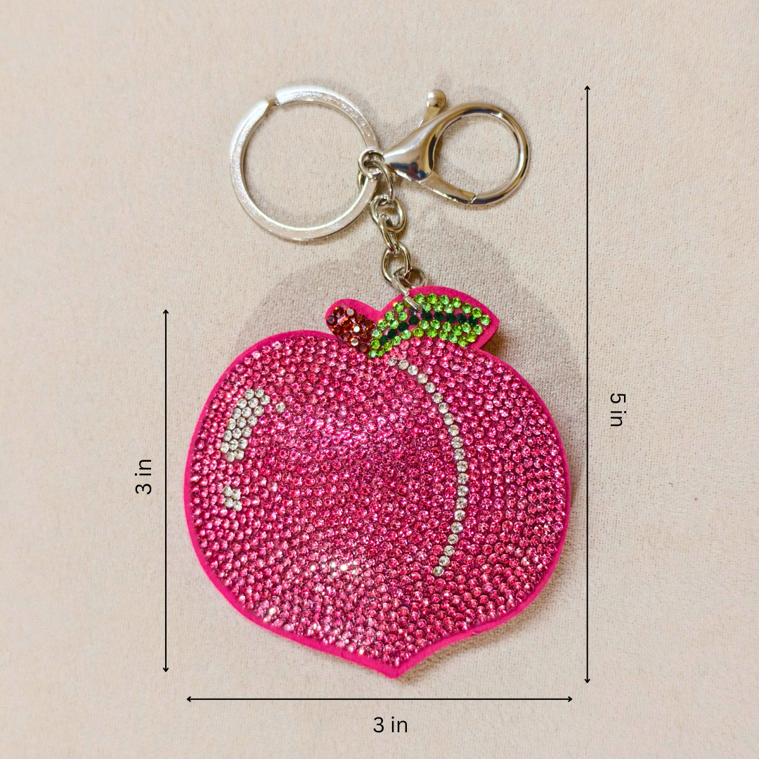 Pink peach-shaped keychain with gemstones on a beige background