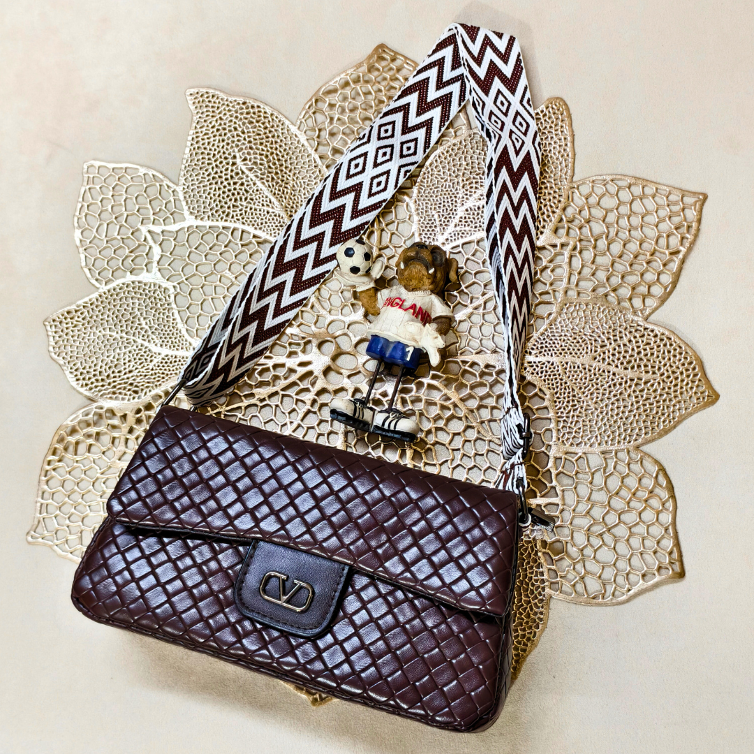 Brown textured handbag with a decorative strap on a textured beige surface