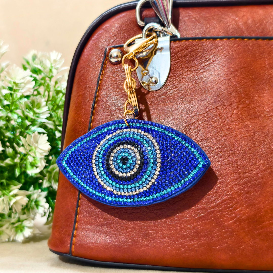 Blue beaded eye keychain on a brown leather bag with a blurred plant in the background
