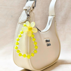 Beige handbag with a yellow flower-shaped keychain on a light background