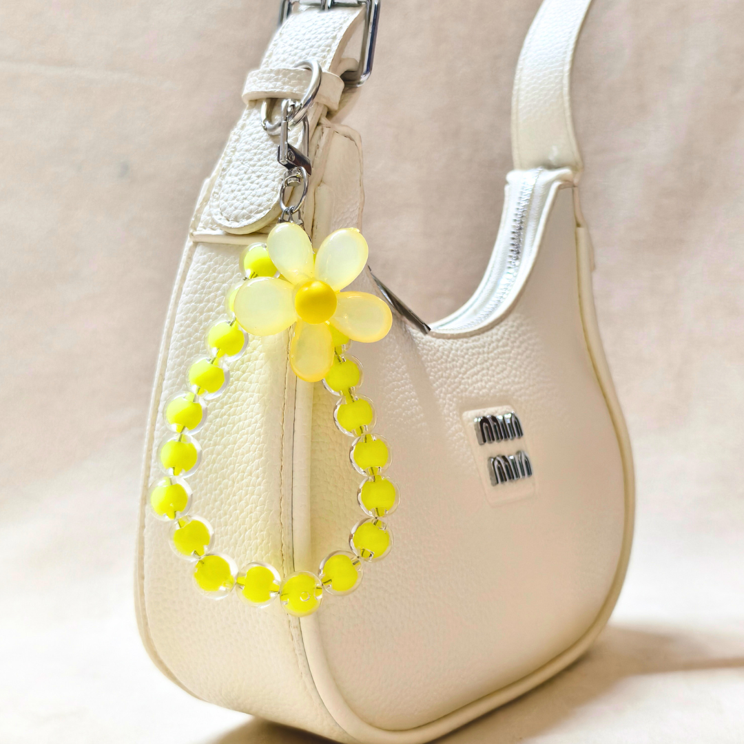Beige handbag with a yellow flower-shaped keychain on a light background