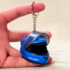 A miniature blue racing helmet keychain held between fingers to show its small scale. The keychain features a silver metal key ring and chain, with 'K-MAX' and 'HELMET' printed in white on the blue helmet body.
