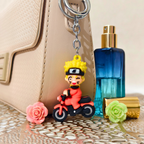 Keychain of a character on a motorcycle next to a blue perfume bottle and flowers.