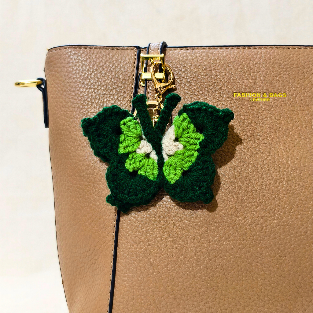 Green butterfly keychain attached to a beige handbag.