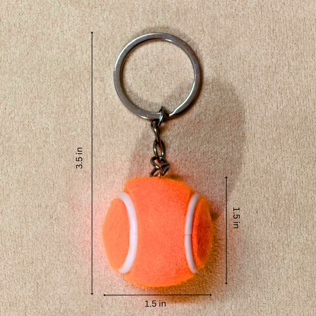 An orange tennis ball keychain with a silver metal split ring and chain, shown on a beige textured background with black dimension lines and text indicating measurements of 1.5 in height, 1.