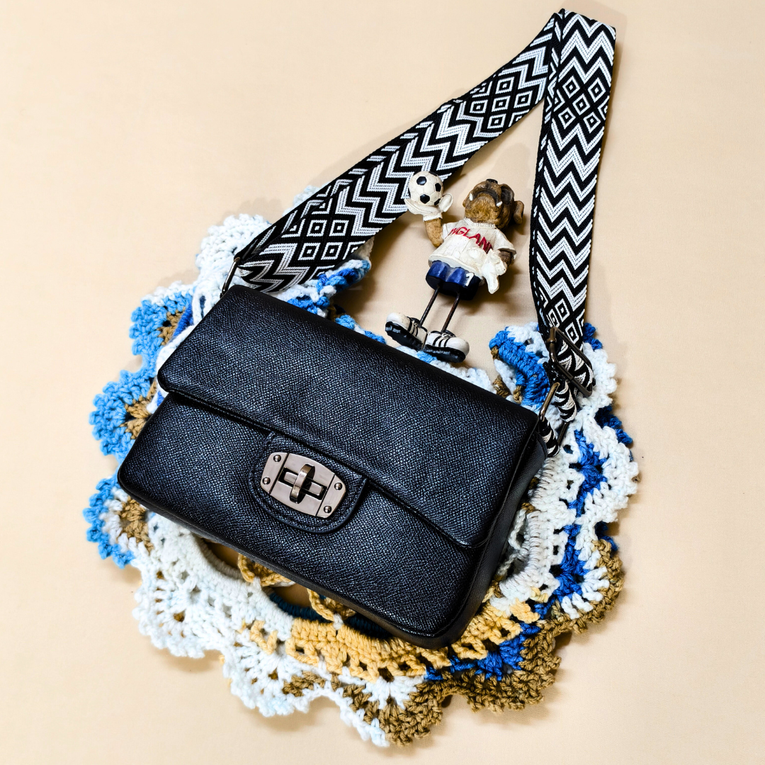 Black handbag with a decorative strap on a textured surface