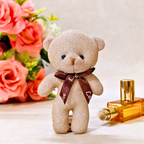 Glittery teddy bear with a brown bow tie next to a perfume bottle and flowers on a light background