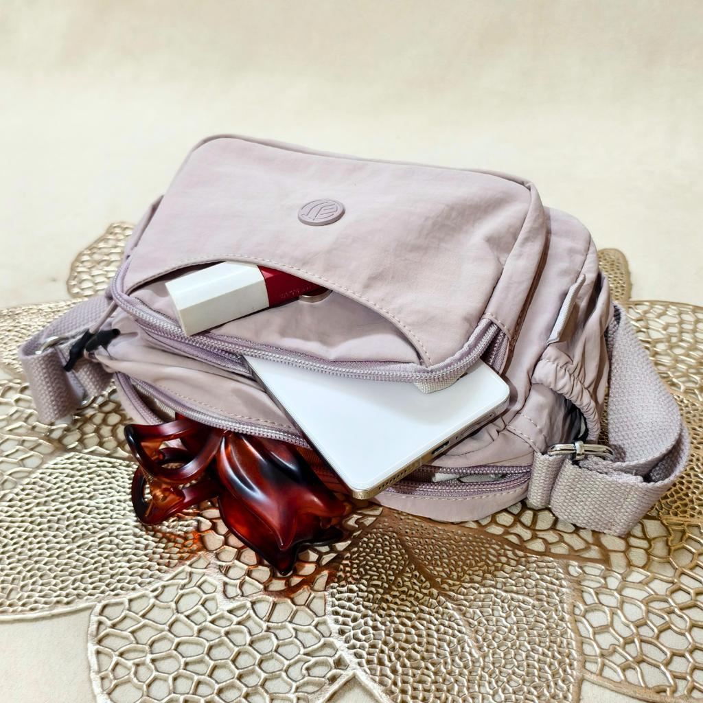 Lavender Lilac Sling Bag With Items In Front Of Beige Background.