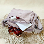 Lavender Lilac Sling Bag With Items In Front Of Beige Background.