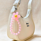 Pink beaded flower keychain attached to a beige handbag.