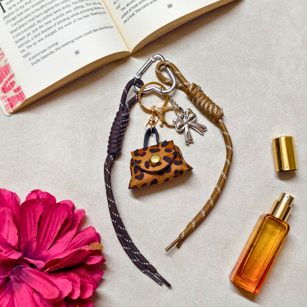 Keychain with leopard print purse charm, book, pink flower, and perfume bottle on a light surface