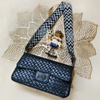 Black woven handbag with a decorative strap on a textured beige surface