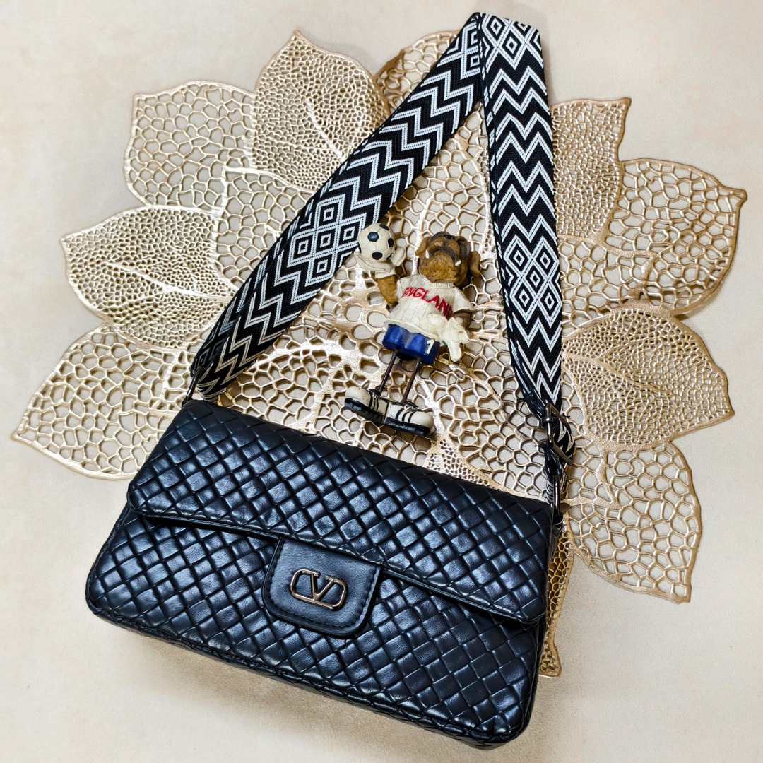 Black woven handbag with a decorative strap on a textured beige surface