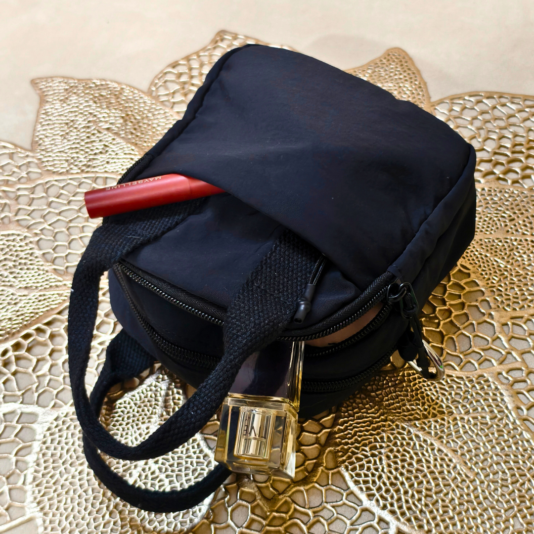 Black handbag with a red lipstick and gold lock on a textured beige surface