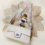 White handbag with decorative ribbon and small toy figure on a textured beige surface