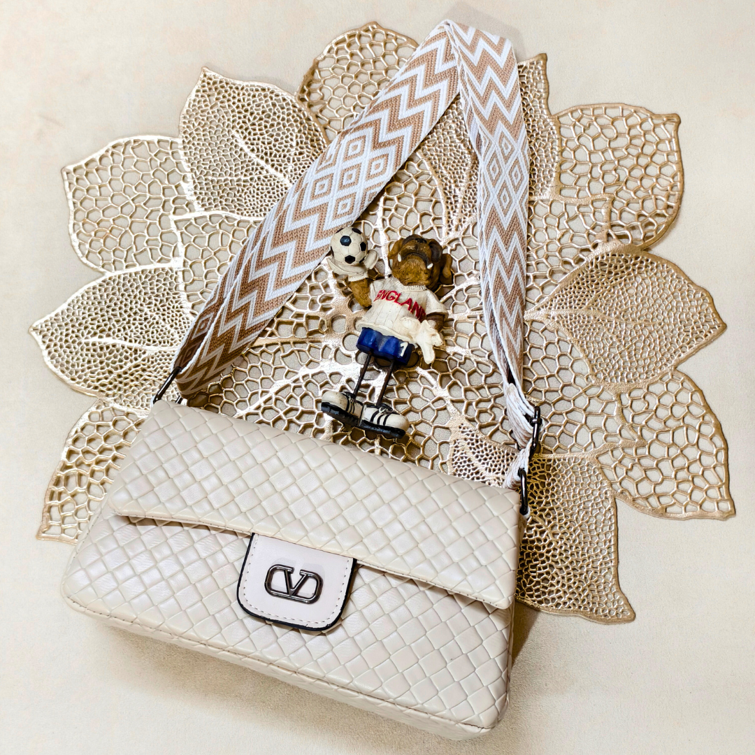 White handbag with decorative ribbon and small toy figure on a textured beige surface