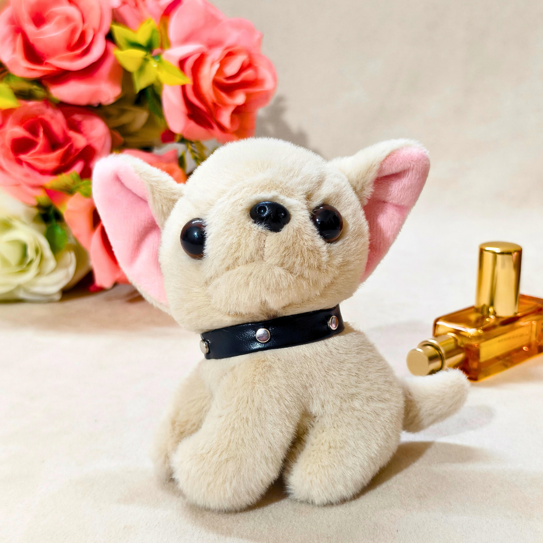 Plush dog toy with a black collar next to a perfume bottle and flowers on a light surface.