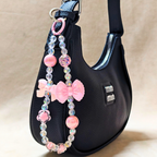 Pink Bow Charm Attached on Hand Bag In Front Of Beige Background.