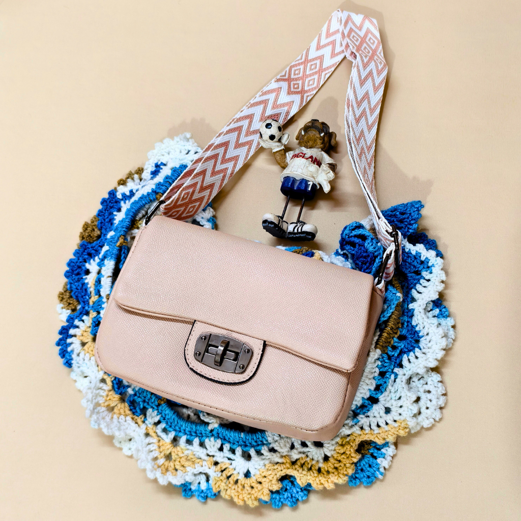 Beige handbag with a decorative strap on a colorful crocheted surface