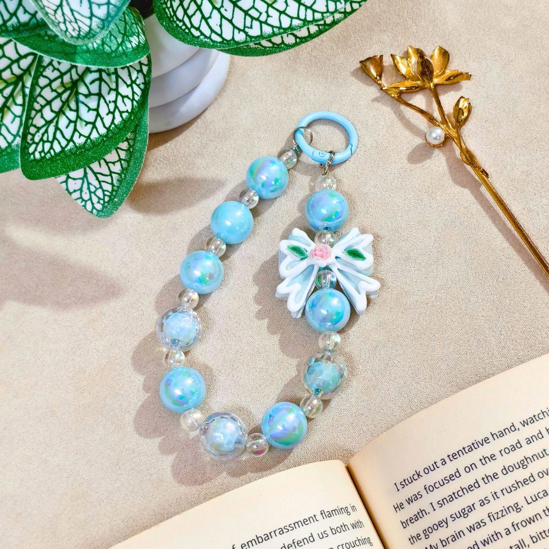 Blue beaded bracelet with a decorative flower charm on a textured surface with green leaves and a gold flower.