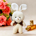 White teddy bear with bunny ears next to a perfume bottle and flowers on a light background