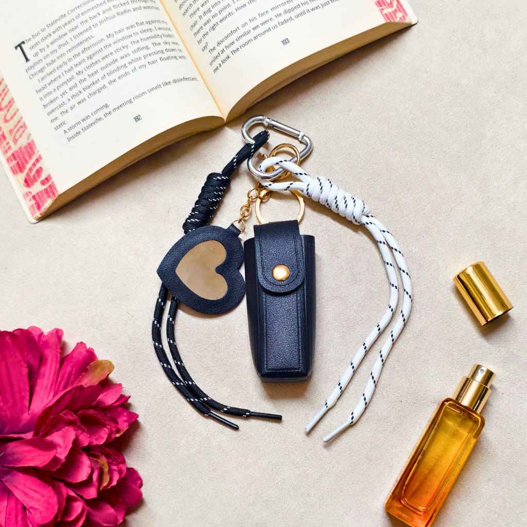 Keychain with heart-shaped tag and leather pouch on a surface with a book and flower.
