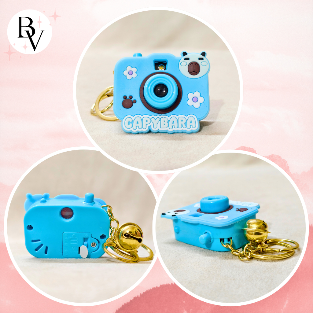 Capybara-shaped blue camera keychain with gold chain on a pink background