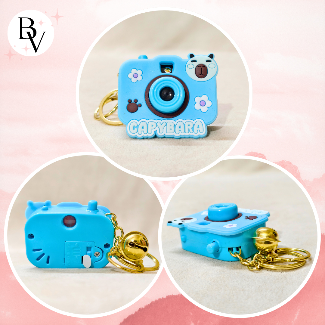 Capybara-shaped blue camera keychain with gold chain on a pink background