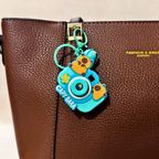 Capybara-themed camera charm on a brown leather bag with 'Fashion & Bags' branding.