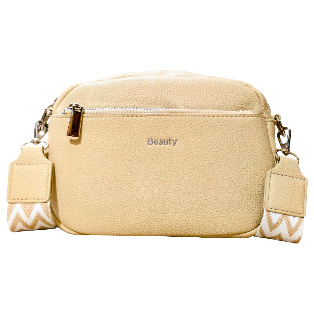 A light beige pebbled faux-leather crossbody bag with a top zipper, a silver-tone metal 'Beauty' logo on the front, and a matching patterned woven strap.