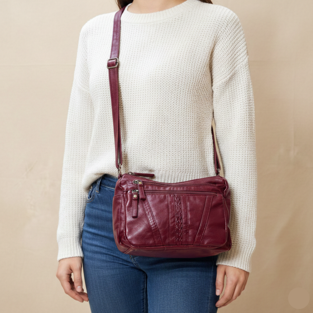 Person wearing a white sweater and blue jeans with a burgundy leather crossbody bag on a beige background