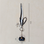 Black and white keychain with a small bag charm on a beige background, showing measurements.