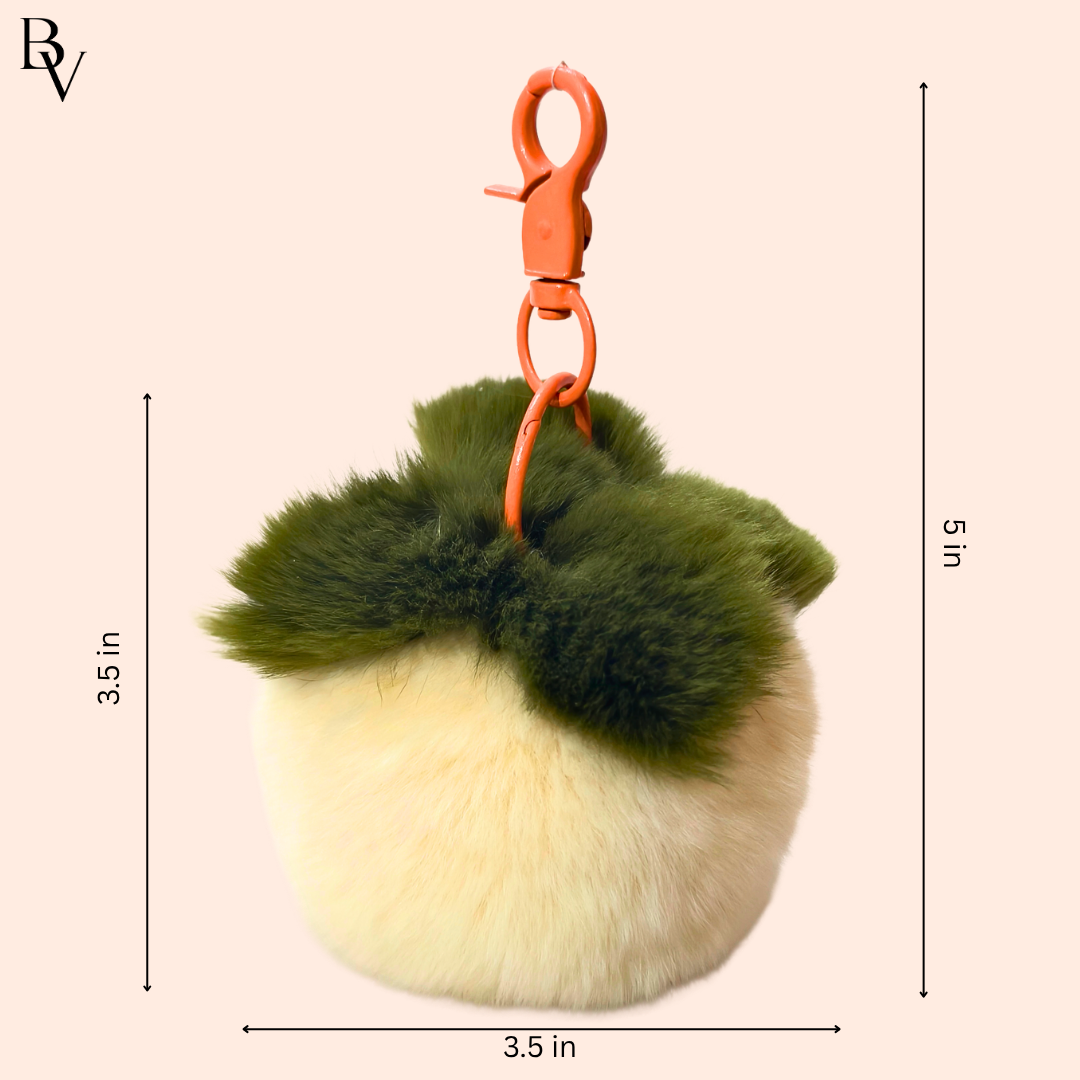 Keychain with green and beige fur balls and an orange clip on a beige background