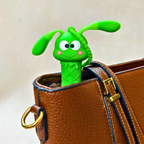 Green cartoon-style rabbit charm peeking out of a brown leather bag.
