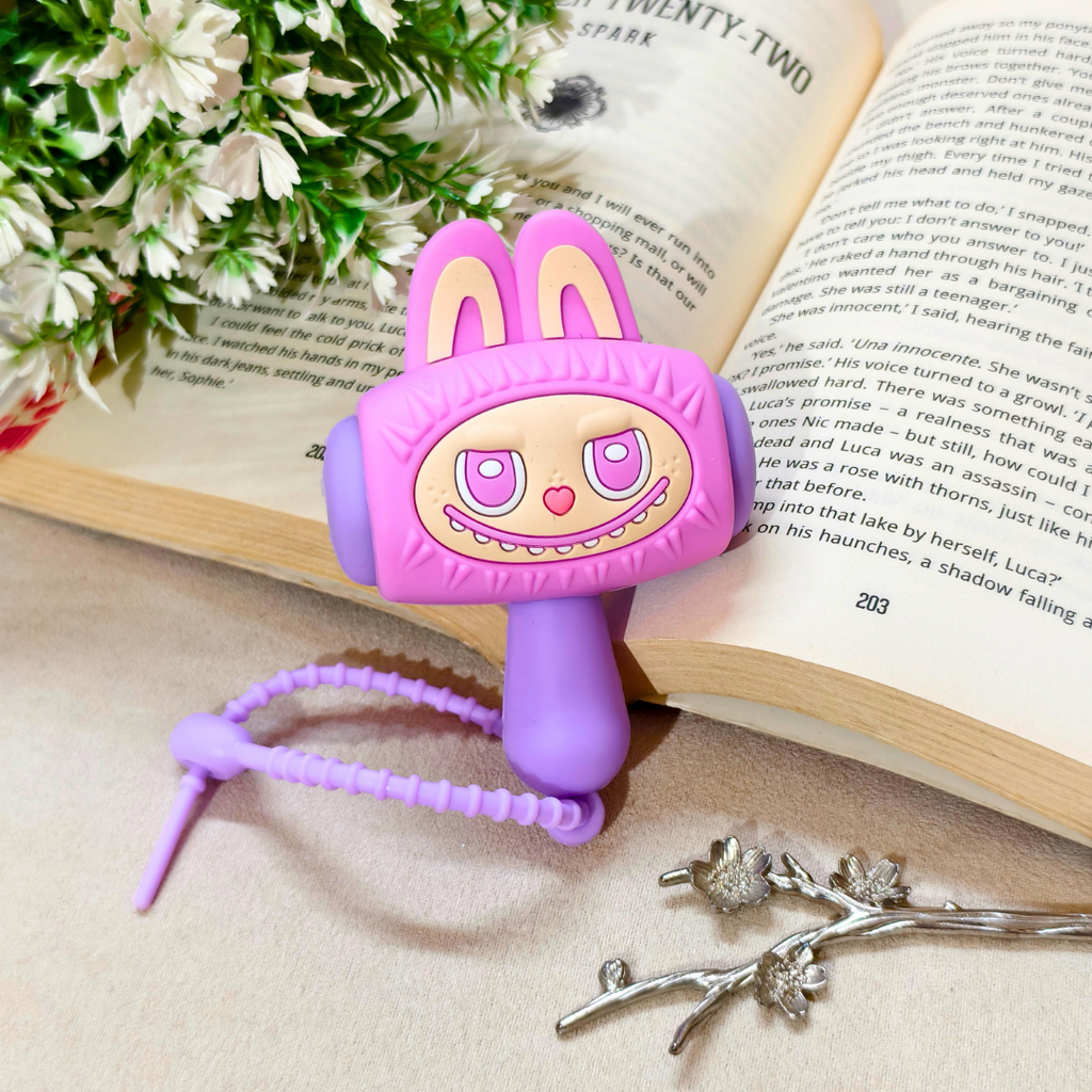 A pink and purple bunny-themed vibrator with a beaded tail, styled on an open book with white flowers and a silver branch.