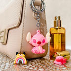 Pink cartoon character keychain on a beige handbag with a bottle of perfume and small toys.