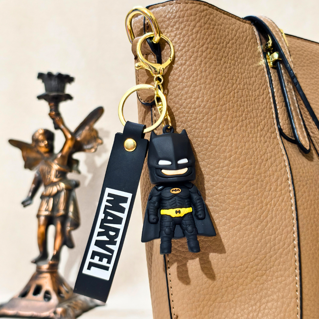 Batman keychain with Marvel tag attached to a beige bag, with a bronze statue in the background.