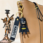 Batman keychain with Marvel tag attached to a beige bag, with a bronze statue in the background.