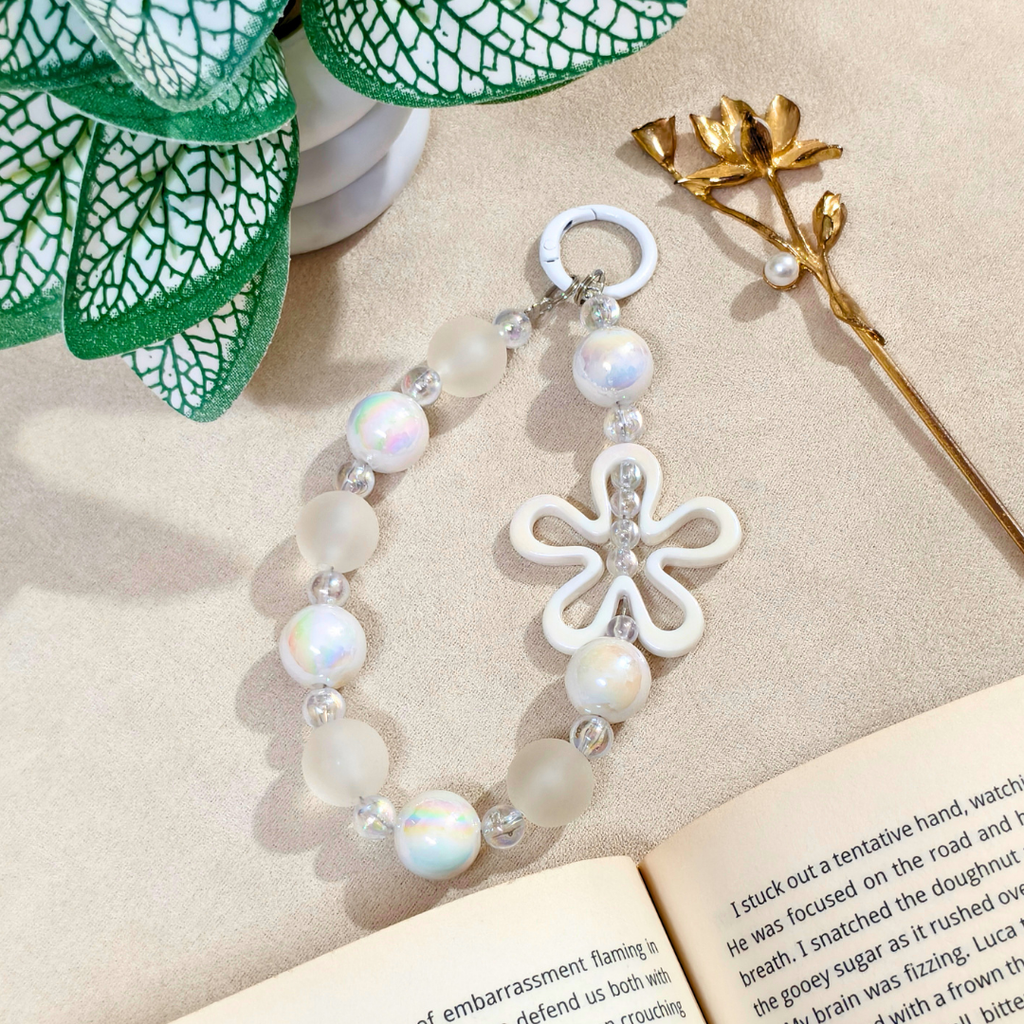 Pearl bracelet with a white flower charm on a beige surface with an open book and decorative elements.